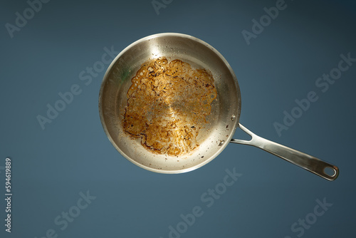 Dirty oily burnt metal frying pan or skillet isolated on a light blue background, no people