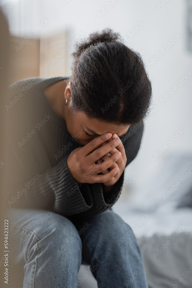 Depressed multiracial woman crying while sitting on bed at home. Depressed multiracial woman crying while sitting on bed at home.
