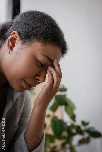 Depressed multiracial woman crying and touching forehead at home.