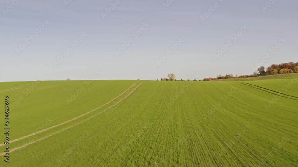 A drone flies over the hill of a field to a small town. The sun is shining. Location: Germany A drone flies over the hill of a field to a small town. The sun is shining. Location: Germany