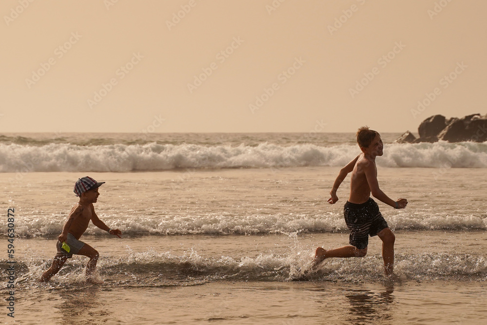 Fototapeta premium Children have fun running on the beach by the water. The brothers are chasing each other