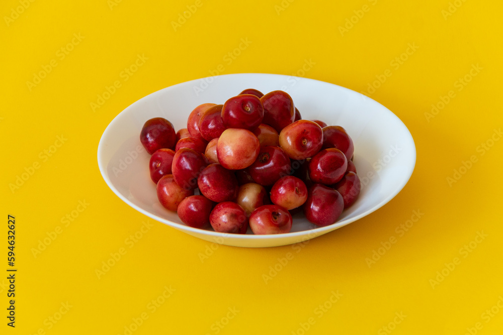 Fresh ripe cherries in a white plate on a yellow background. Healthy food. Vegetarian breakfast. Close-up.
