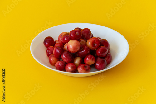 Obraz na płótnie Fresh ripe cherries in a white plate on a yellow background. Healthy food. Vegetarian breakfast. Close-up. w salonie