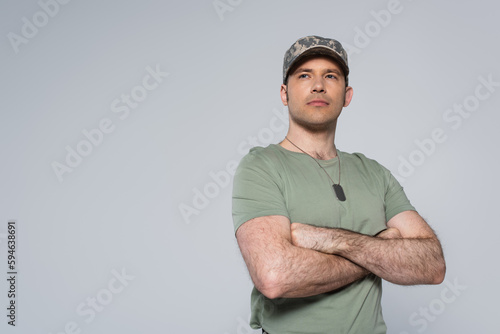 military man in t-shirt and cap standing with folded arms during memorial day isolated on grey. photo