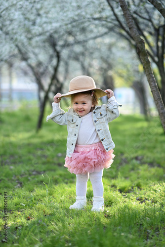 portrait of a cute little girl wearing hat in spring meadow on green grass