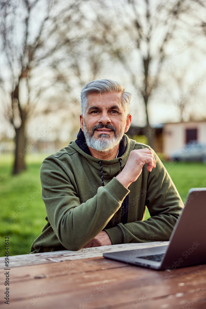 Fototapeta premium Portrait of a smiling senior businessman working over the laptop in nature.