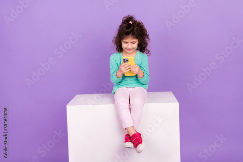Photo of dreamy pretty small kid wear turquoise shirt typing modern device empty space isolated violet color background