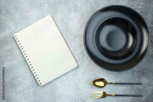 Black dinnerware set and cutlery set spiral notebook on isolated gray ice background with free space