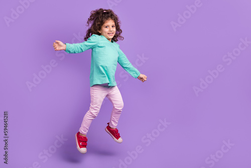 Full length photo of cute adorable small kid wear turquoise shirt jumping high empty space isolated violet color background