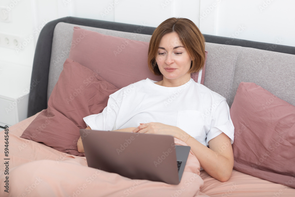 Attractive woman lying in the bed and working on laptop Attractive woman lying in the bed and working on laptop