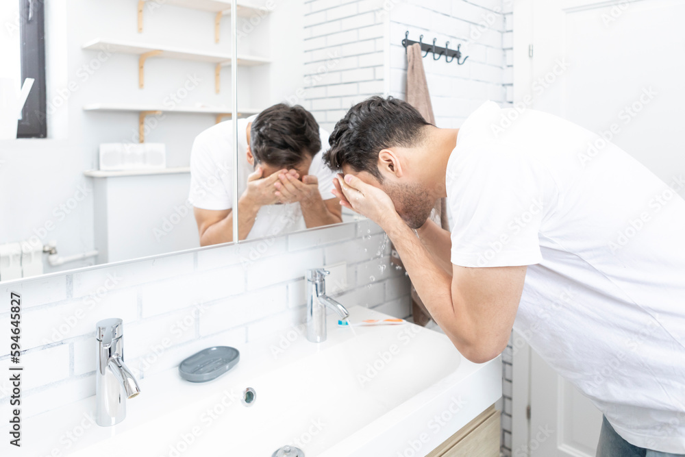 Handsome man washing his face in the bathroom. Morning routine and hygiene concept Handsome man washing his face in the bathroom. Morning routine and hygiene concept