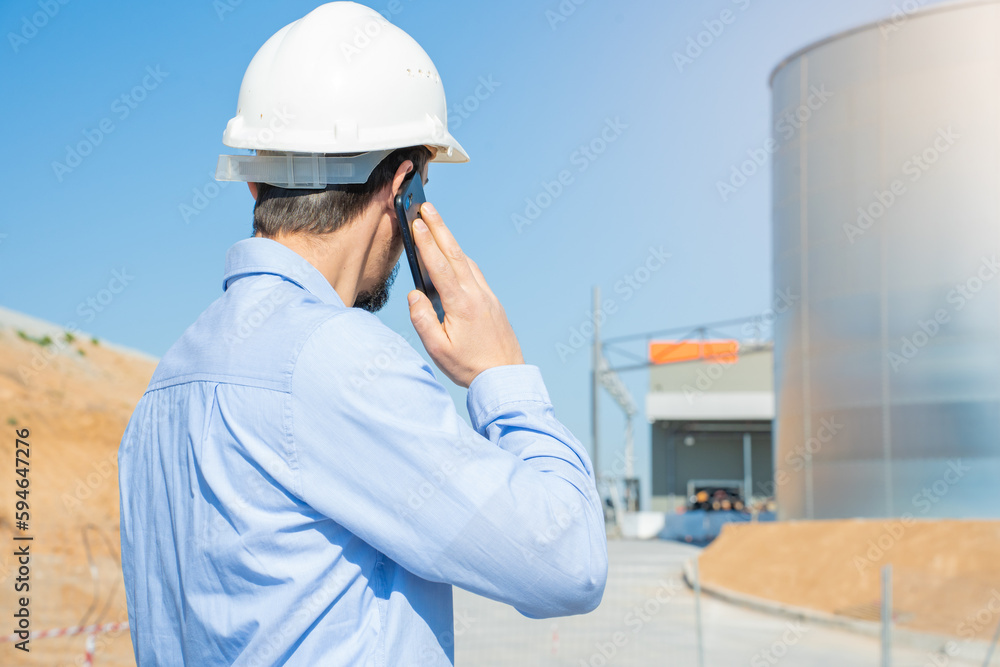 Civil engineer inspecting work, call to supervisor with smartphone standing outdoors at construction Civil engineer inspecting work, call to supervisor with smartphone standing outdoors at construction