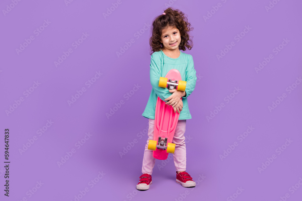 Photo of positive shiny little child dressed teal shirt holding penny board empty space isolated purple color background