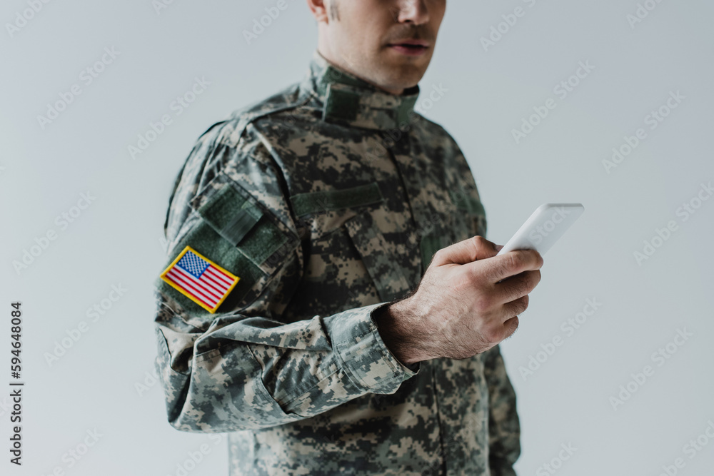 cropped view of American serviceman using smartphone isolated on grey.