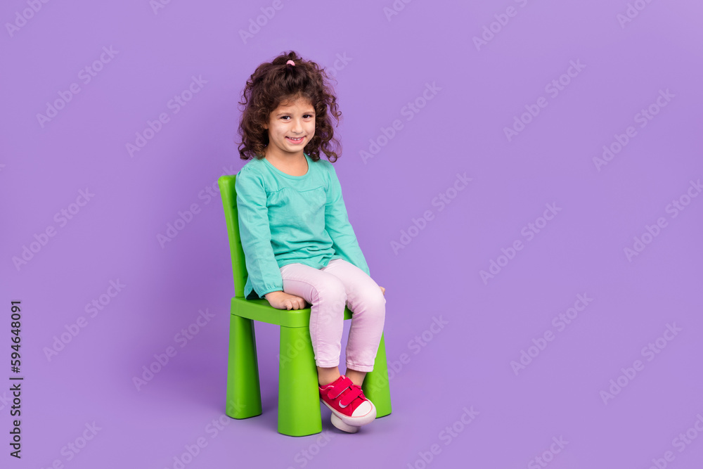 Full length photo of pretty charming little child dressed teal shirt sitting chair empty space isolated purple color background Full length photo of pretty charming little child dressed teal shirt sitting chair empty space isolated purple color background