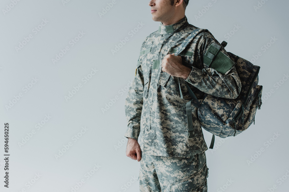 Fototapeta premium cropped view of serviceman in army uniform standing with backpack isolated on grey.