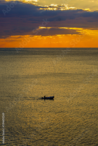 kleines Boot auf offenem Meer in der roten Abendsonne hinter Wolken