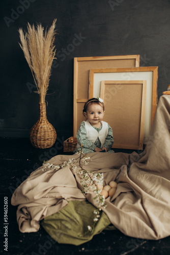 Little cute girl with paints and eggs in a studio with beautiful decorations and spring flowers and picture frames