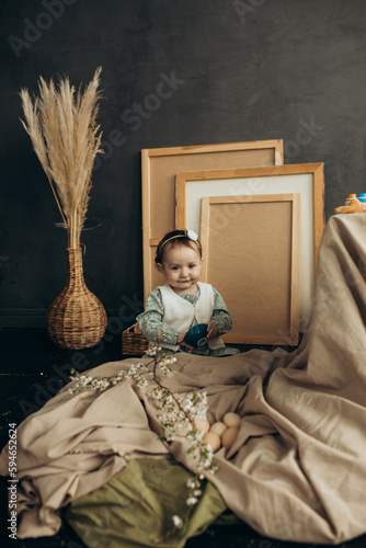 Little cute girl with paints and eggs in a studio with beautiful decorations and spring flowers and picture frames