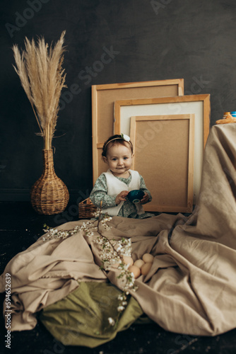 Little cute girl with paints and eggs in a studio with beautiful decorations and spring flowers and picture frames