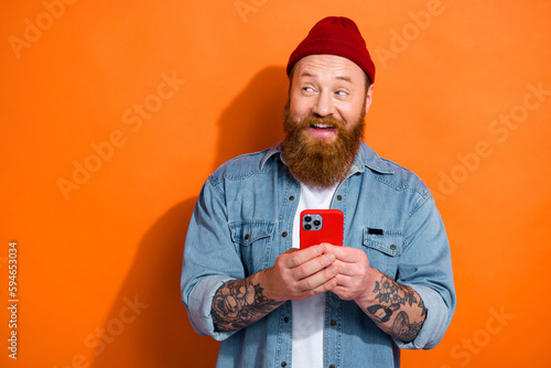 Photo of funky cheerful man wear jeans shirt chatting modern device gadget looking empty space isolated orange color background