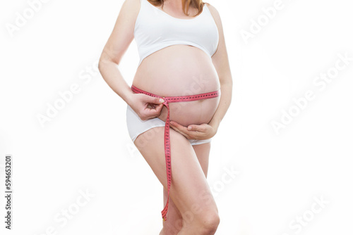 Młoda piękna ciężarna dziewczyna mierzy jej brzuch taśmą w domu. Koncepcja zdrowej ciąży.  Białe tło, Ciężarna szczęśliwa kobieta dotyka jej brzucha. Portret kobiety w ciąży w średnim wieku. 