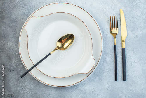 Elegant spoon in empty white soup plates and fork knife on half dark light gray background with distressed surface with free space