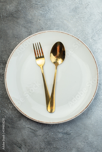 Golden cutlery set on white plate on gray background with distressed coarse-grained gradient surface photo