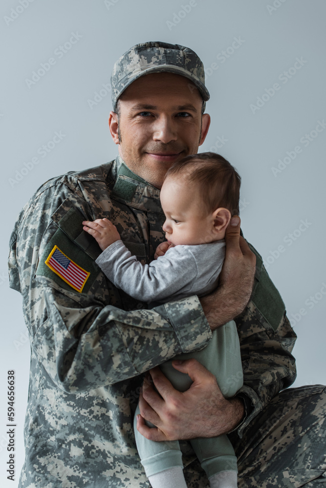 happy US soldier in uniform holding in arms newborn boy isolated on grey. happy US soldier in uniform holding in arms newborn boy isolated on grey.