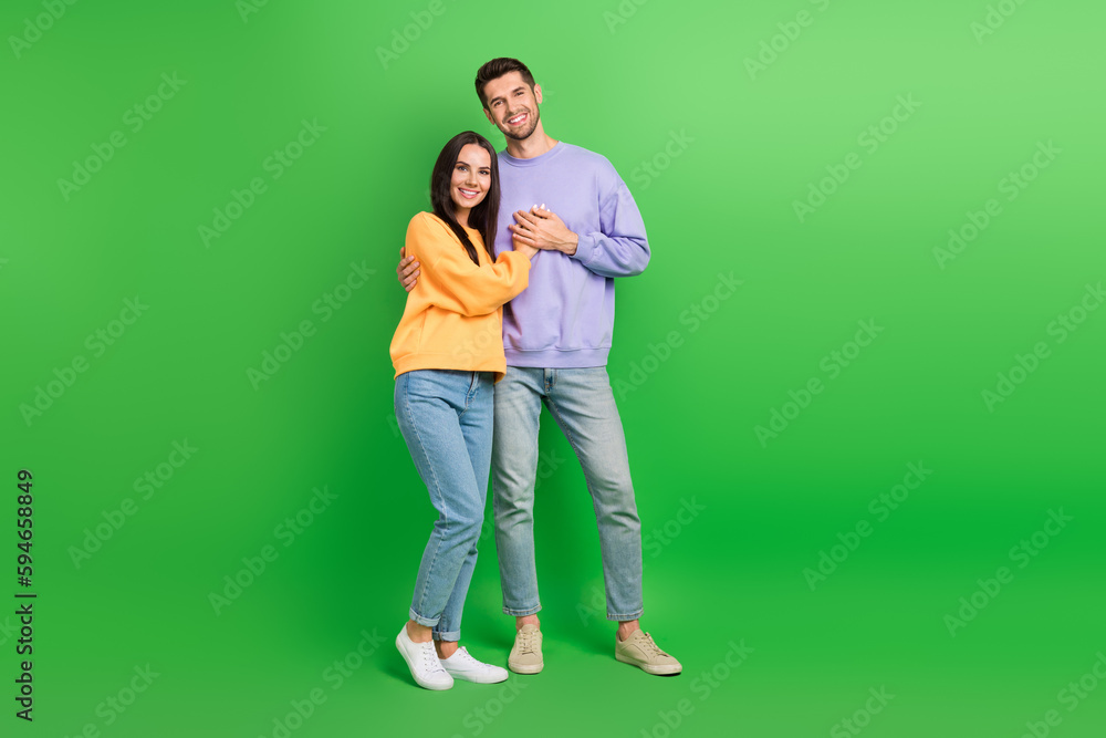 Full length photo of pretty shiny husband wife dressed sweatshirts cuddling isolated green color background