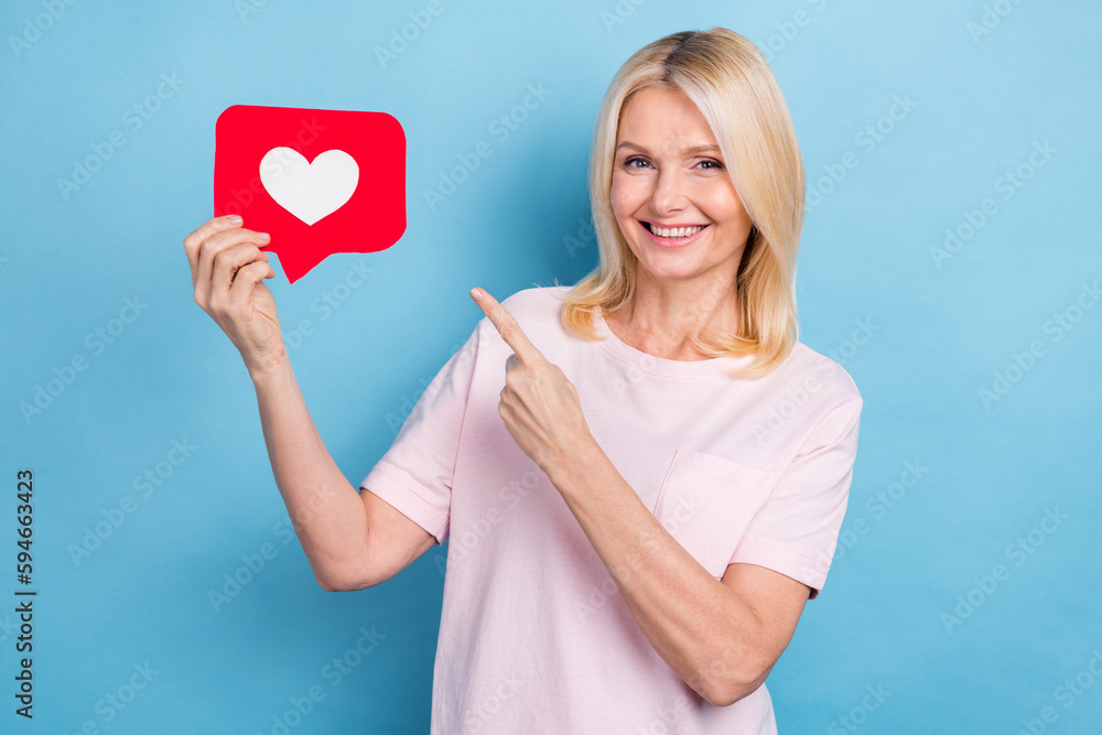Portrait of cheerful senior woman with straight hairdo wear white t-shirt directing at like icon isolated on blue color background Portrait of cheerful senior woman with straight hairdo wear white t-shirt directing at like icon isolated on blue color background