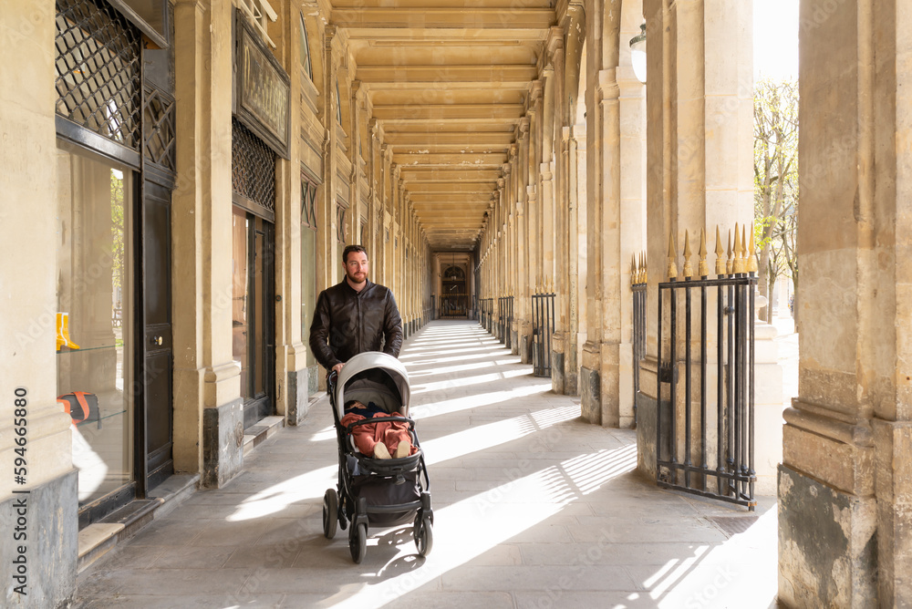 Obraz premium Father pushing his sleeping daughter in a stroller in the galleries of the Palais-Royal in Paris.