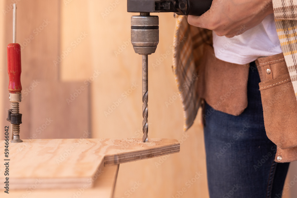 Crop carpenter drilling hole in wooden plank with electric screwdriver in home carpentry shop during workday