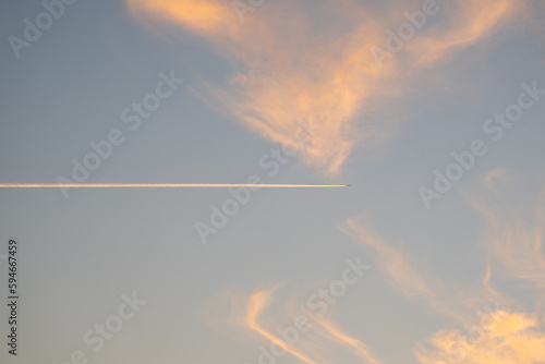 Plane flying between the clouds creating condensation clouds, at sunset.