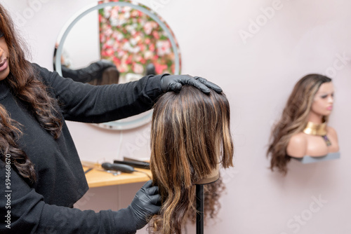 african american Hairdresser fitting mannequin head with oncologic wig photo