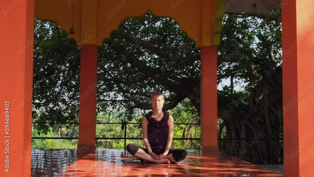 Inspired european woman meditates sitting on the floor in yoga temple, breathing deeply with closed eyes. Sunlight illuminates her face. Basic female practice for mental health. Inspired european woman meditates sitting on the floor in yoga temple, breathing deeply with closed eyes. Sunlight illuminates her face. Basic female practice for mental health.