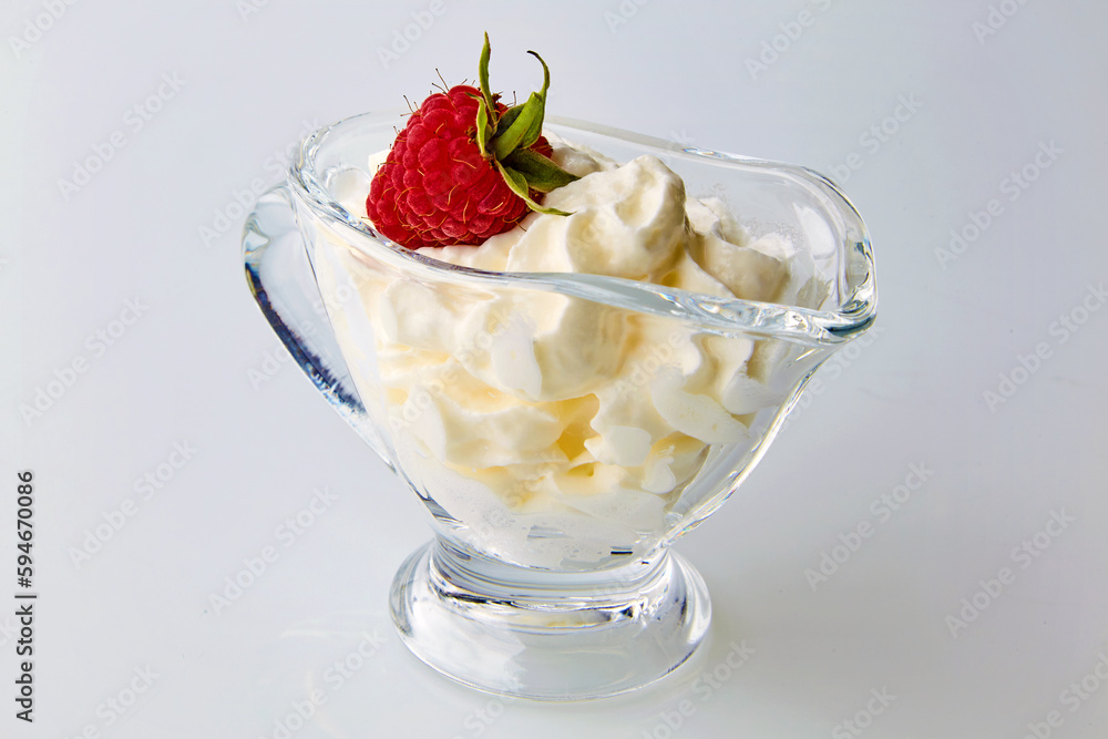 Red raspberries in a glass gravy boat with cream on a white background Red raspberries in a glass gravy boat with cream on a white background