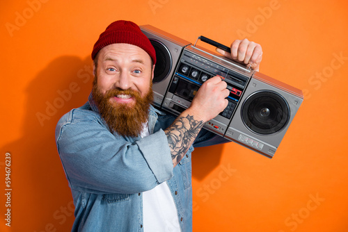 Photo of cheerful positive man wear jeans shirt turning on boom box music isolated orange color background