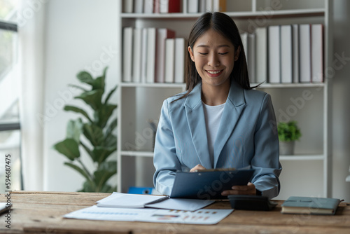 Asian businesswoman, investor, insurance salesman looking with pen pointing at data sheet on financial performance showing graphs Finance on real estate project on chart at desk in office.