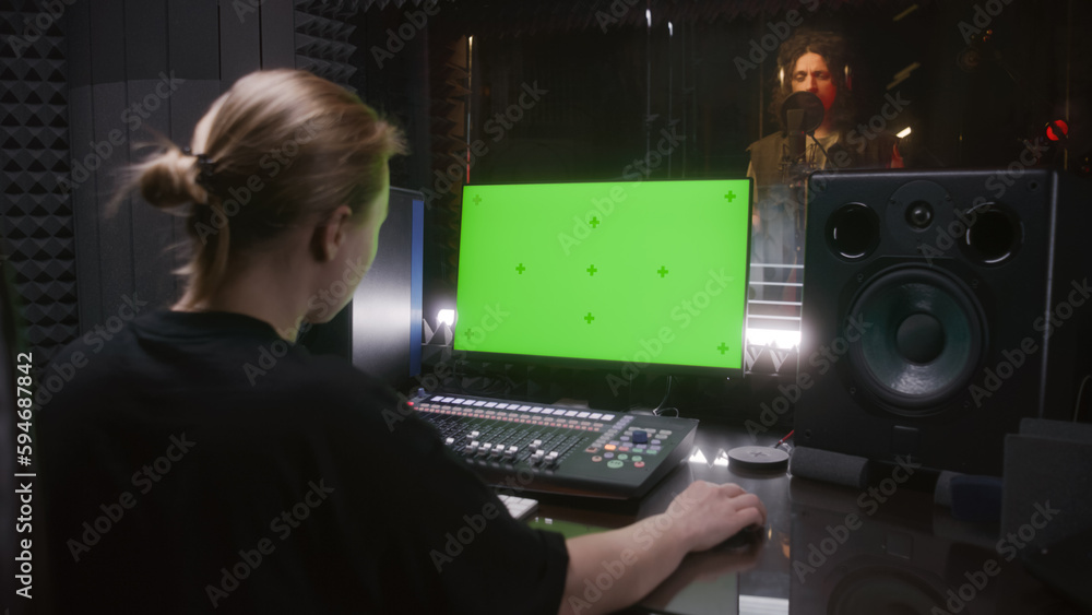 Male singer records song in soundproof room. Female audio engineer, producer uses control mixing surface. Computer screen showing DAW software with sound tracks. Sound recording studio. Green screen. Male singer records song in soundproof room. Female audio engineer, producer uses control mixing surface. Computer screen showing DAW software with sound tracks. Sound recording studio. Green screen.