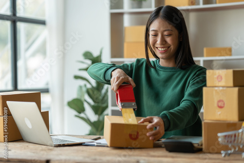 starting a small business Asian young woman business owner using masking tape to stick Close the parcel box, prepare for delivery through the shipping company according to the received online order. © crizzystudio
