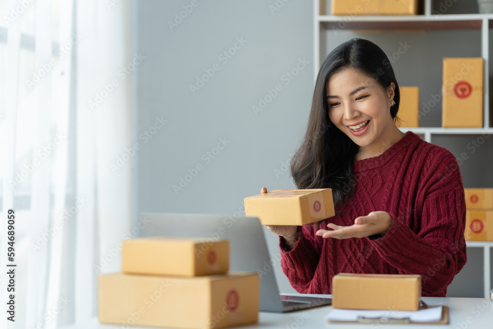 Small business startup images SME business owner, female entrepreneur talking online via laptop to check orders and prepare sales boxes for customers. Online SME business concept. Small business startup images SME business owner, female entrepreneur talking online via laptop to check orders and prepare sales boxes for customers. Online SME business concept.