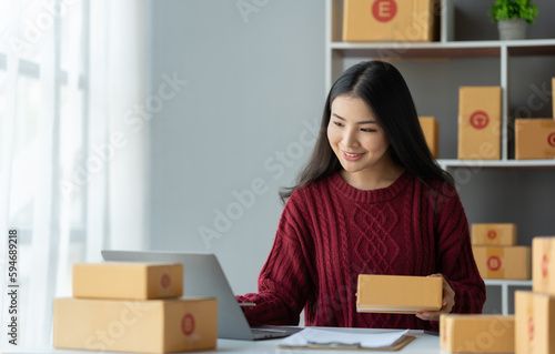 Online business ideas Asian businesswoman holding parcel boxes preparing to deliver to customers with joy. © crizzystudio