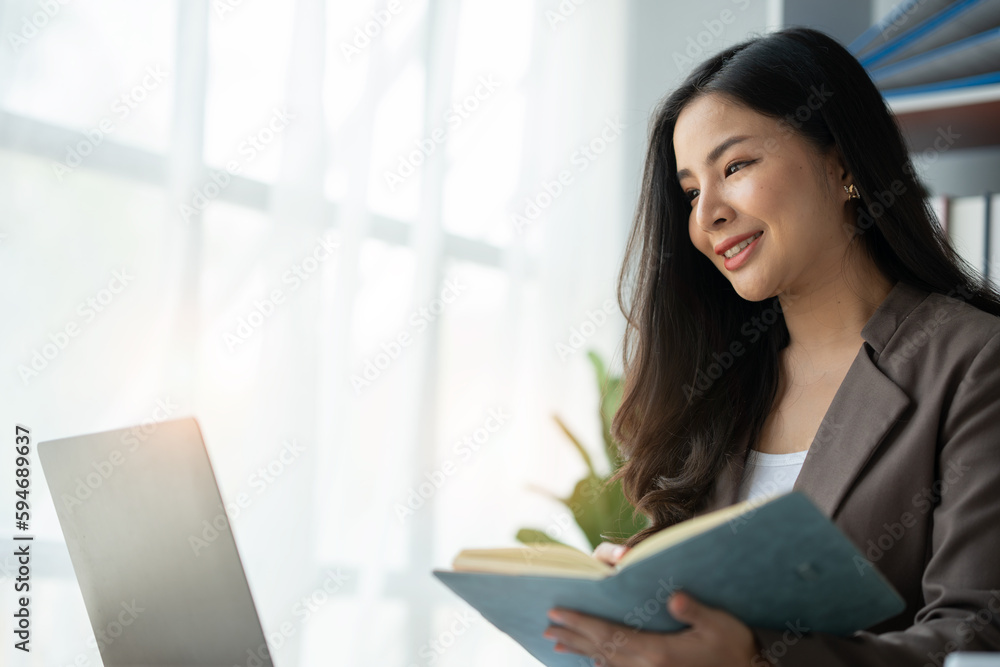 Asian businesswoman logging in a notebook looking at laptop computer for analyzing marketing strategies and real estate tax information for clients accounting and tax concepts. Asian businesswoman logging in a notebook looking at laptop computer for analyzing marketing strategies and real estate tax information for clients accounting and tax concepts.