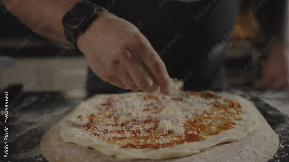 Slow motion of the chef pouring cheese on the pizza before putting it in the oven Slow motion of the chef pouring cheese on the pizza before putting it in the oven