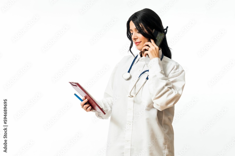 Young Caucasian female speaking on phone while holding a clipboard and pen on a white background. Young Caucasian female speaking on phone while holding a clipboard and pen on a white background.