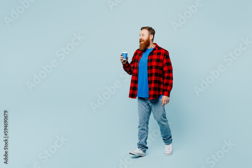 Full body young redhead bearded man wear casual clothes hold takeaway delivery craft paper brown cup coffee to go isolated on plain pastel light blue cyan background studio portrait Lifestyle concept