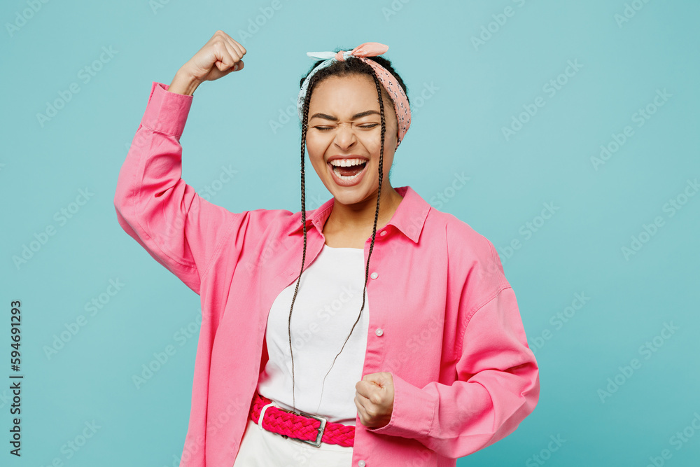 Young fun woman of African American ethnicity wear pink shirt white t-shirt headscarf doing winner gesture celebrate clenching fists say yes isolated on plain pastel light blue cyan background studio. - obrazy, fototapety, plakaty 