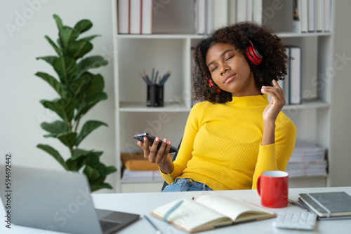 Startup businesswoman, American woman African woman wearing headphones music and holding mobile phone using bluetooth listening music while sitting resting after work happily and relaxing at office.
