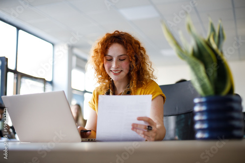 Beautiful businesswoman with orange hair working on laptop in her office